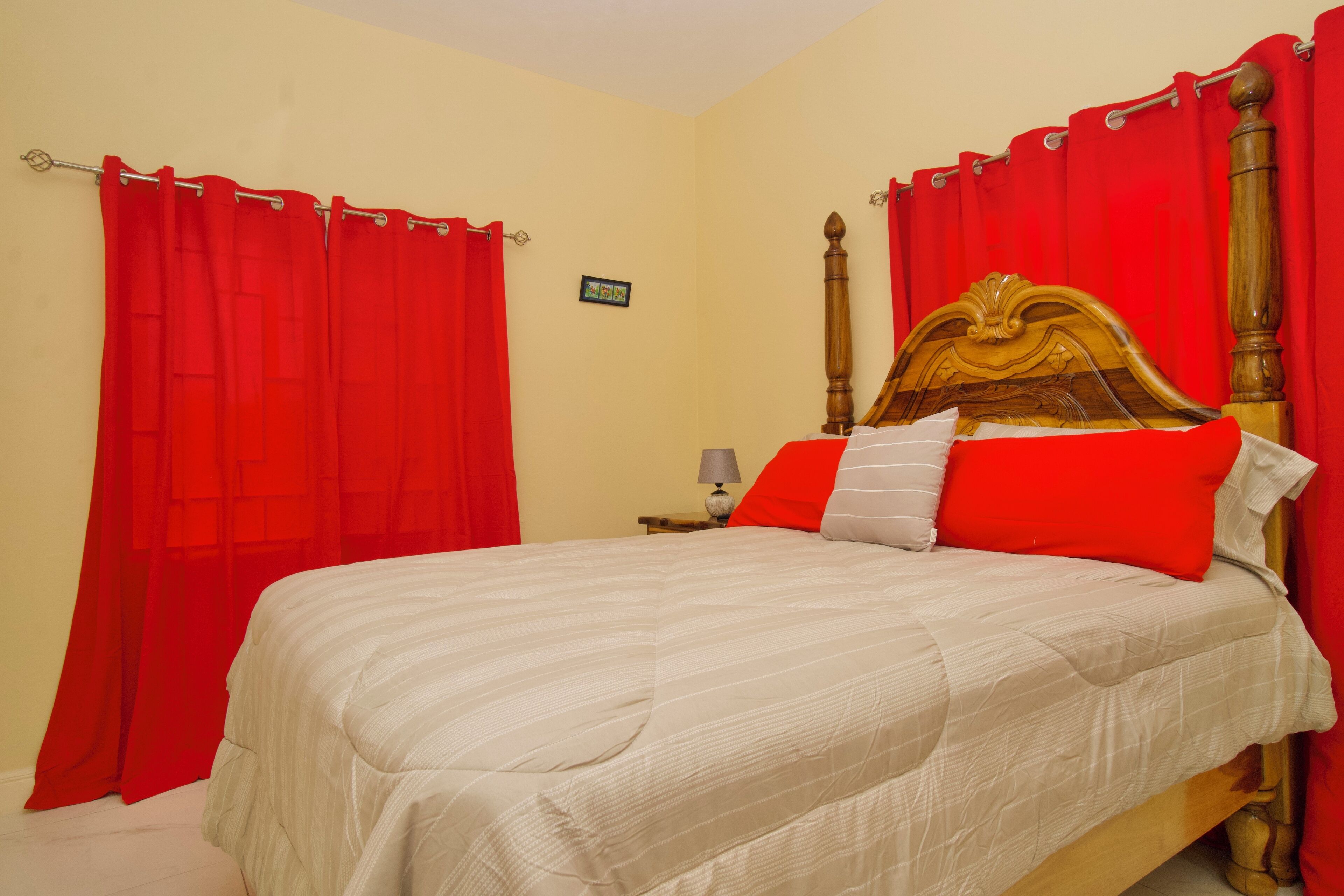 Una cama con cabecera de madera, cortinas rojas y colcha blanca.