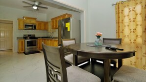 Un comedor con una mesa redonda, sillas, un ventilador de techo y una cocina al fondo.