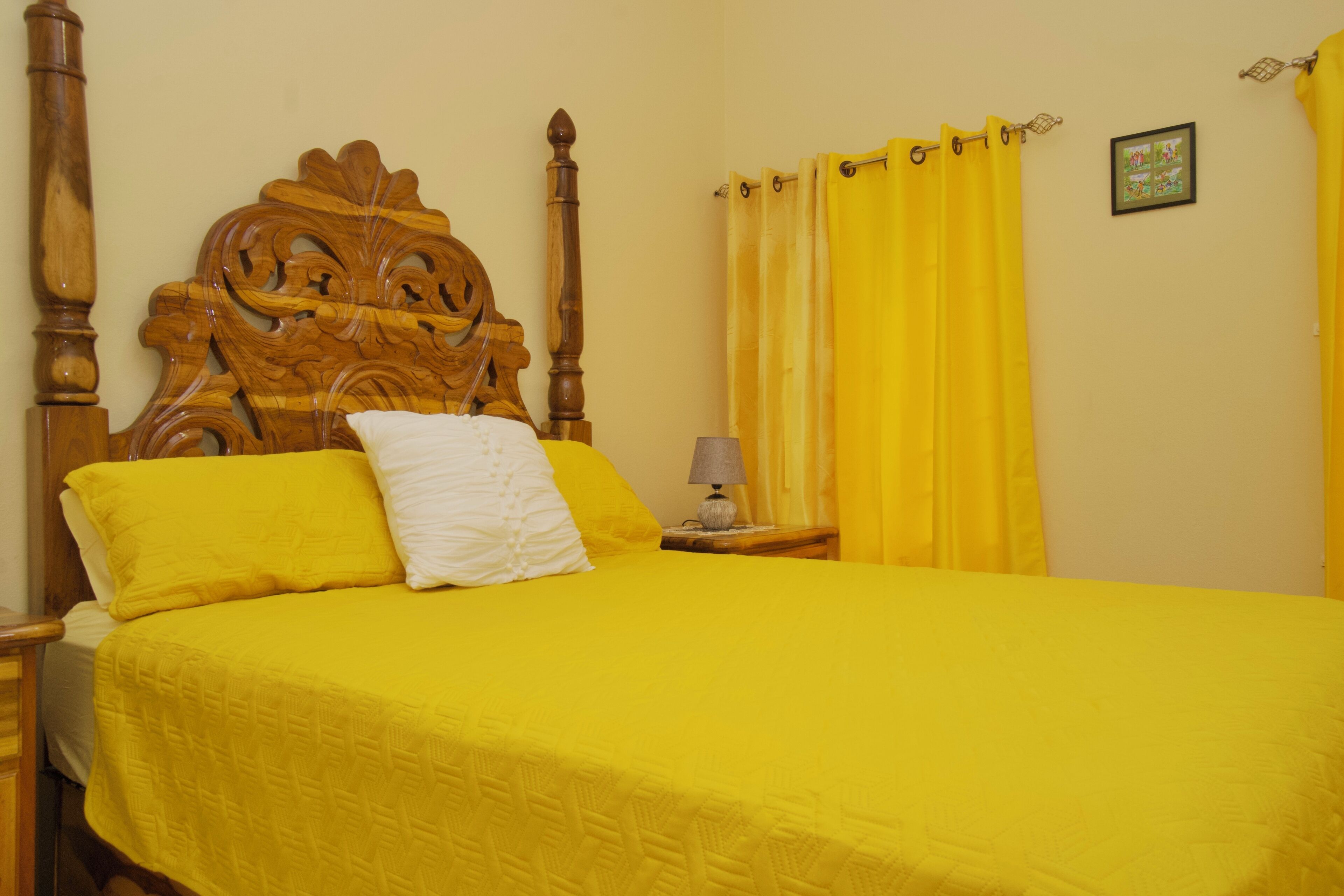 A bed with a wooden headboard, yellow bedding, and a bedside lamp.