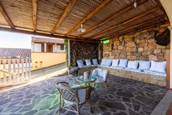 Un patio al aire libre con suelo de piedra, muebles de mimbre y una pared de piedra con cojines.