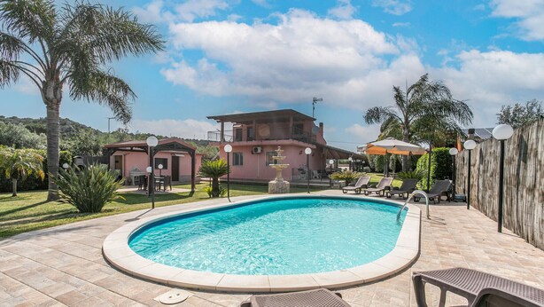 A swimming pool with lounge chairs, a gazebo, and a two-story house in the background.