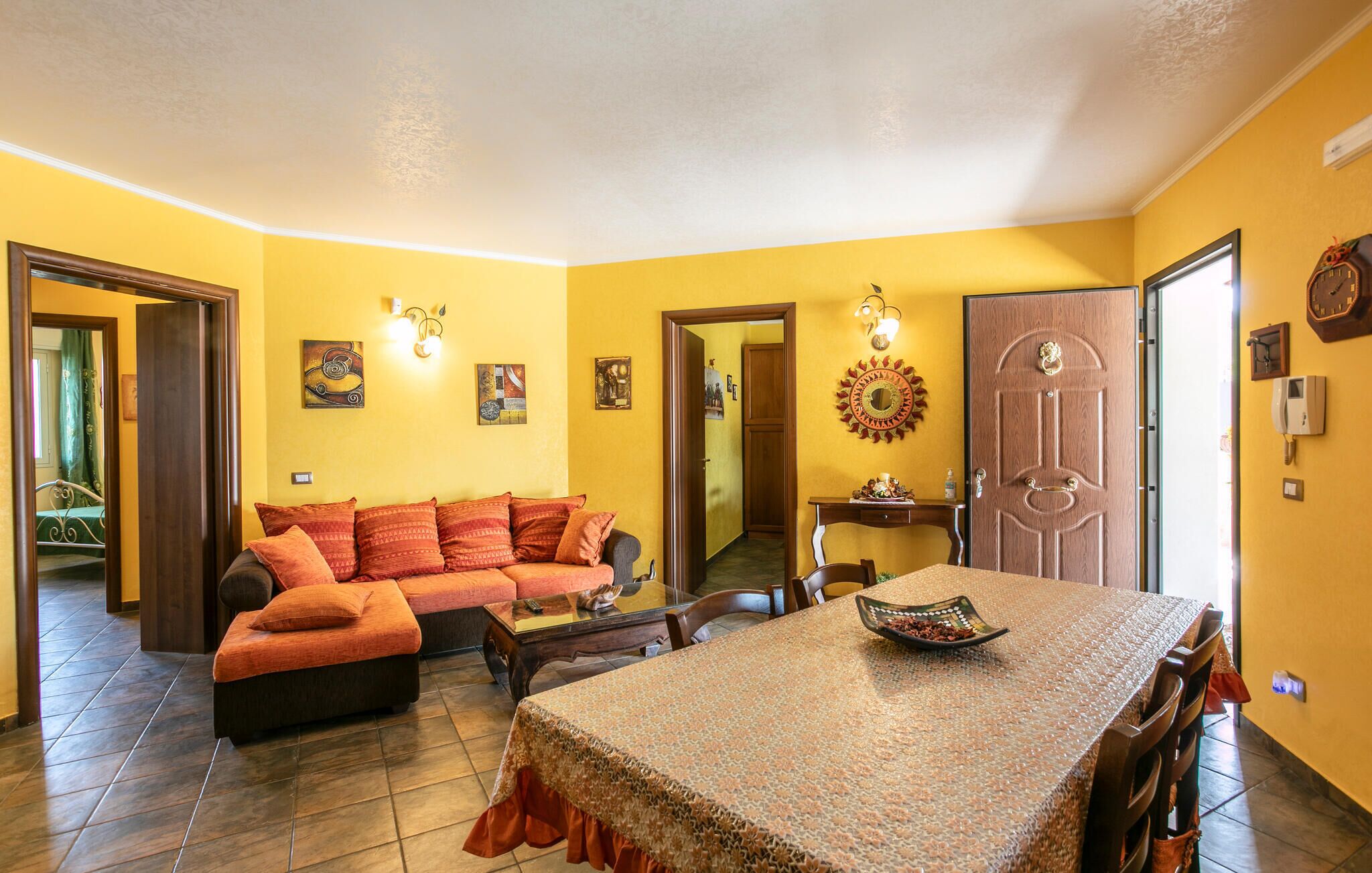 Un salon avec un canapé, une table à manger recouverte d’une nappe à motifs et une porte dotée d’une poignée décorative.