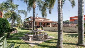 A house with a patio, surrounded by palm trees and a well-maintained lawn.