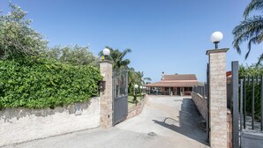 A gated entrance to a property with a paved driveway leading to a covered patio area.
