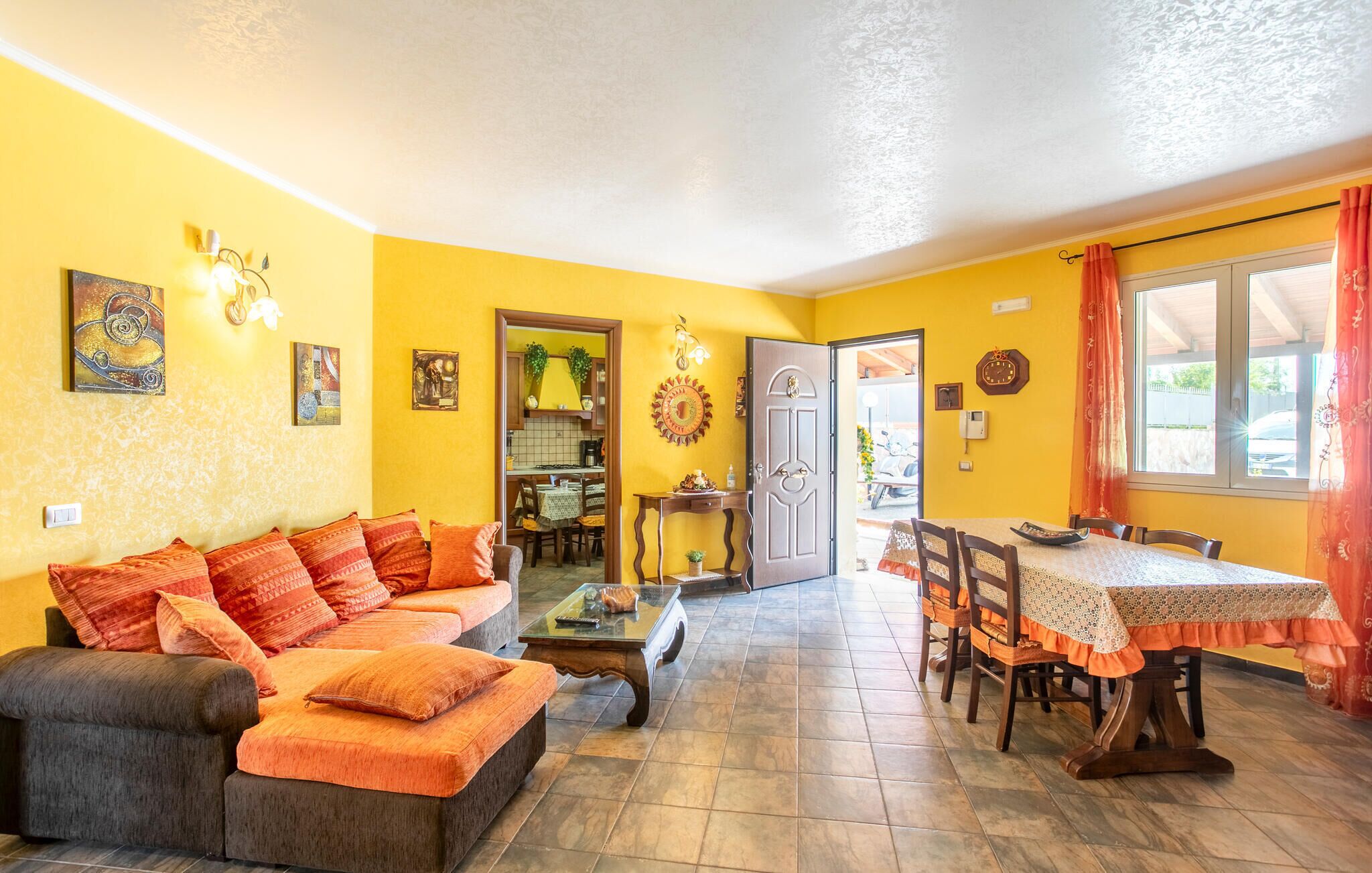 A living room with a sofa, coffee table, and dining table. There is a kitchen visible through an open door.