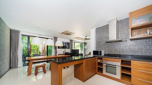 A modern kitchen with wooden cabinets, a black countertop, and a built-in oven. - Pool villa in rawai  (Tambon Rawai)