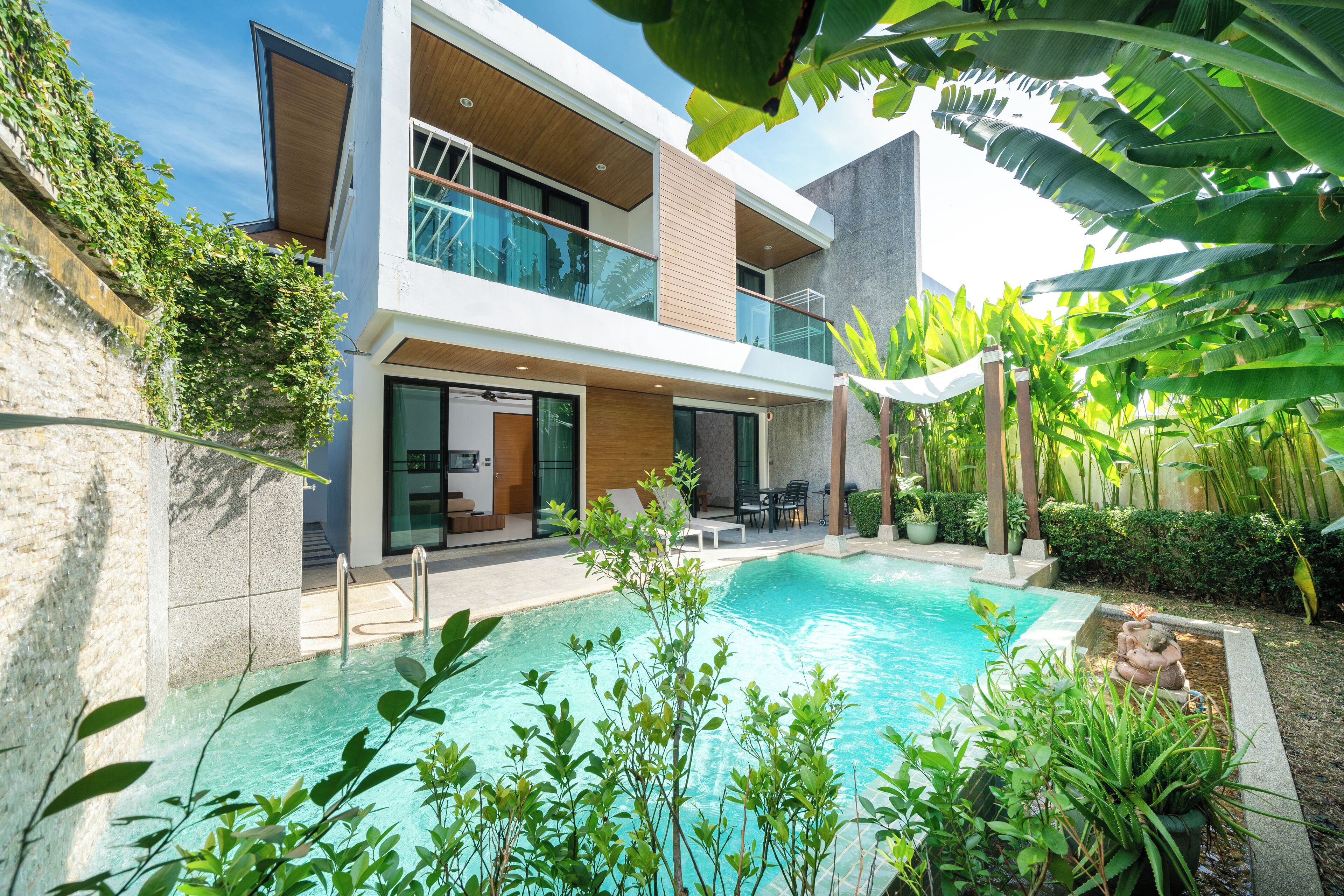 A modern two-story house with a swimming pool, outdoor seating, and lush greenery.