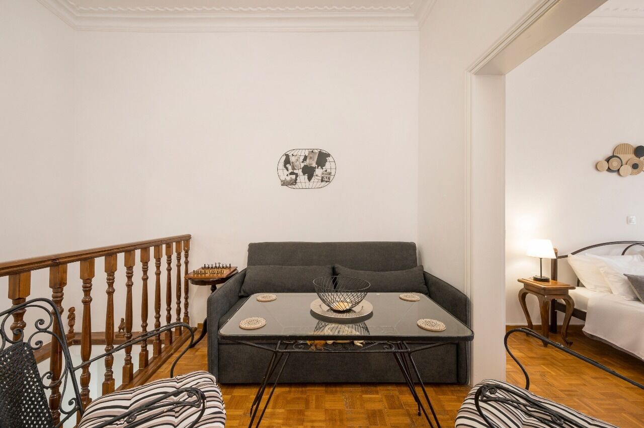 A living room with a grey sofa, a small round table with a decorative bowl, a chessboard, and a wall-mounted abstract art piece.