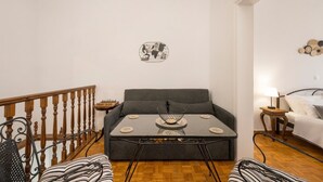 A living room with a grey sofa, a small round table with a decorative bowl, a chessboard, and a wall-mounted abstract art piece. - Lion's Yard (Chania)