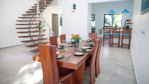 A dining area with a wooden table set for four, surrounded by chairs. A staircase is visible to the left, leading to another level. - Coral Reef Villas (Watamu)