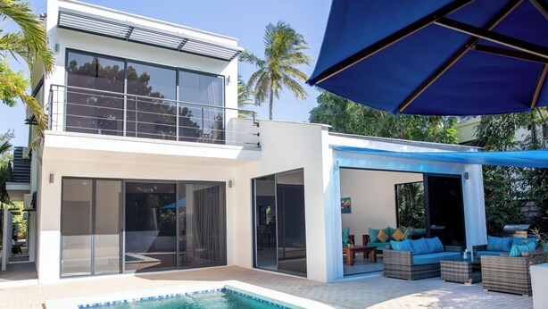 A modern two-story house with a swimming pool, outdoor seating area, and large windows. - Coral Reef Villas (Watamu)