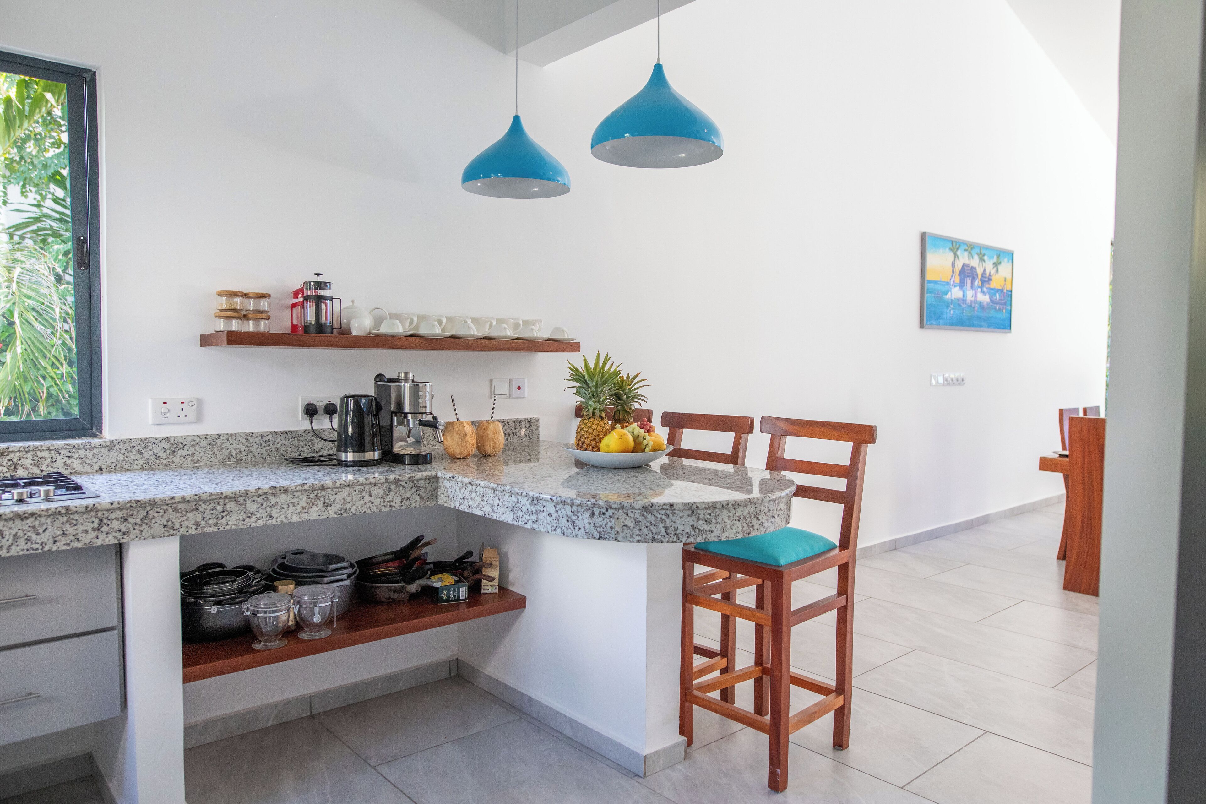 A kitchen with granite countertops, wooden chairs, and blue pendant lights.