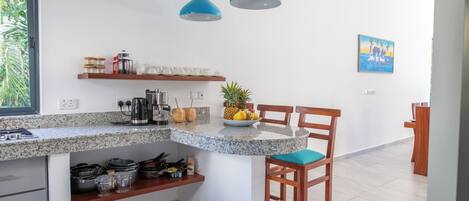 A kitchen with granite countertops, wooden chairs, and blue pendant lights.