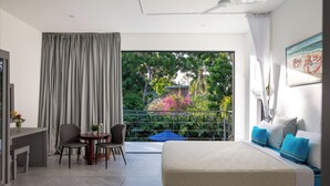 A modern hotel room with a large bed, a dining area with chairs, a small table, and a balcony with a view of greenery and a beach. - Coral Reef Villas (Watamu)