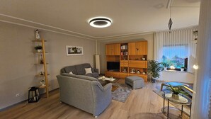 A living room with a grey sofa, wooden bookshelf, TV stand, and a small table with a plant. - Vacation apartment Ernebibbel - comfortable apartment with terrace (Altendiez)