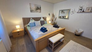 A neatly arranged bedroom with a wooden bed, bedside tables, a bench, and a bedside lamp. - Vacation apartment Ernebibbel - comfortable apartment with terrace (Altendiez)