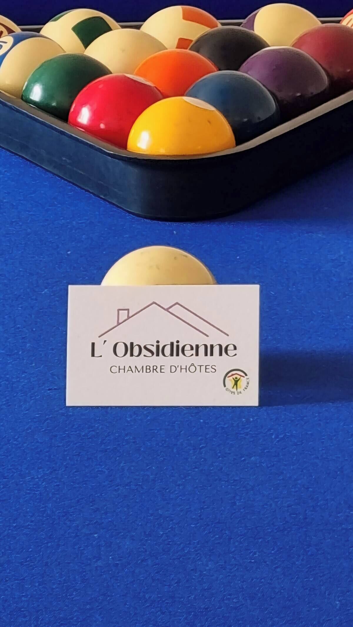 Un tavolo da biliardo con diverse palle colorate e un cartello con su scritto "L'Obsidienne Chambre d'Hôtes".