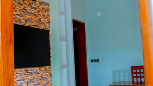 Une pièce avec un mur dont le motif est constitué de briques, une horloge, une porte rouge, une petite table et une chaise.