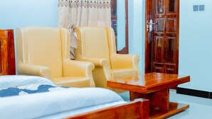 Une chambre d’hôtel avec un lit, deux fauteuils jaunes, une table basse en bois et une armoire en bois.