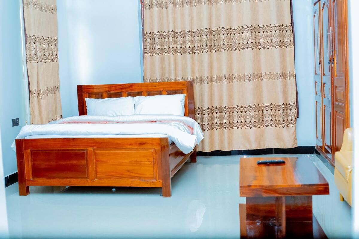 A neatly made bed with a wooden headboard, a bedside table, and curtains with a geometric pattern.