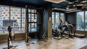 A modern gym with various exercise equipment, large windows, and a view of a cityscape.