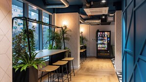 A modern bar area with wooden stools, potted plants, and a vending machine.