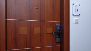 Une porte en bois dotée d’un clavier pour le verrouillage, d’une plaque indiquant le numéro de la chambre et d’un interrupteur sur le mur.