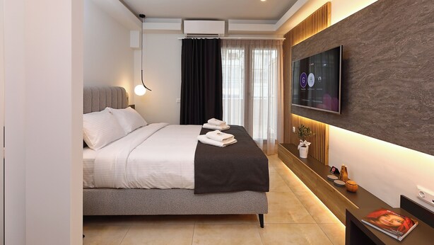 Une chambre d’hôtel moderne équipée d’un lit, d’un téléviseur fixé au mur et d’un comptoir de réception avec quelques magazines.