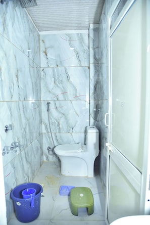 Une petite salle de bain avec des murs en marbre, des toilettes, une douche et un lavabo.
