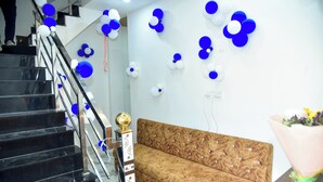 A staircase with black steps and a metal railing, a wooden sofa with a patterned backrest, and a wall decorated with blue and white balloons. - Hotel Sindur (Ujjain)