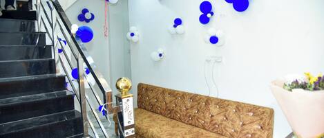 Un escalier avec des marches noires et une rampe en métal, un canapé en bois avec un dossier à motifs et un mur décoré de ballons bleus et blancs.