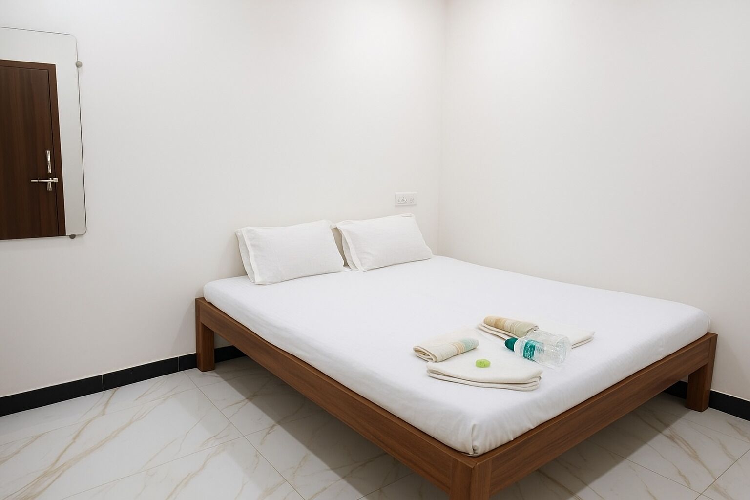 A neatly made bed with white linens and pillows, a wooden frame, and a small towel and bottle on the bed.