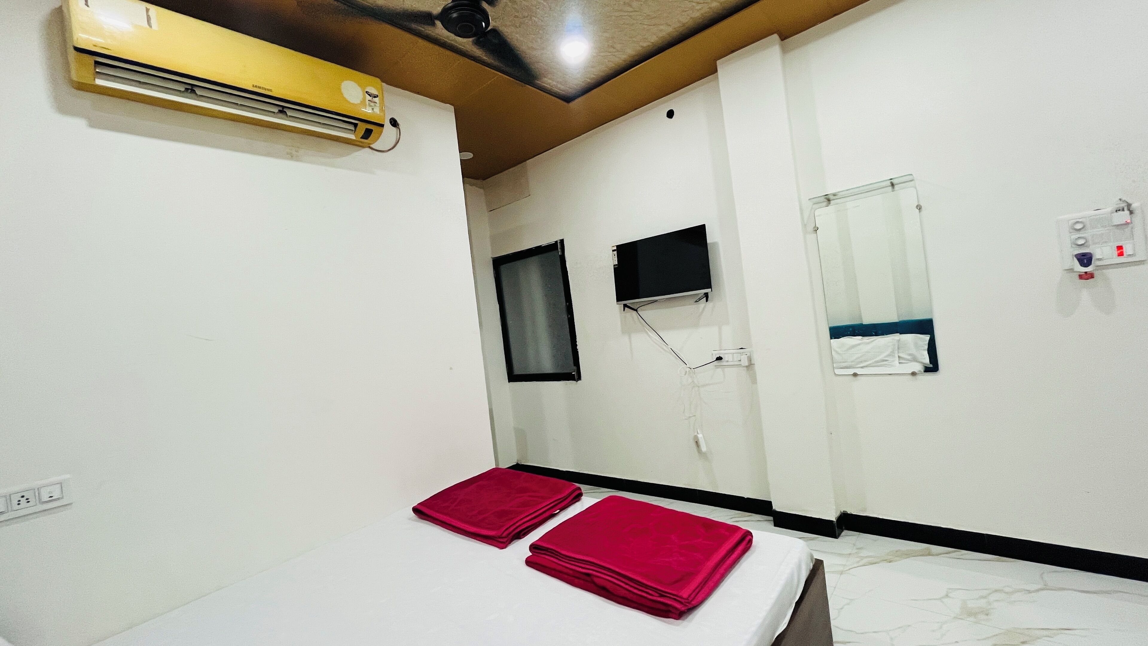 A room with a bed, a wall-mounted TV, a ceiling fan, and a wall-mounted air conditioner.