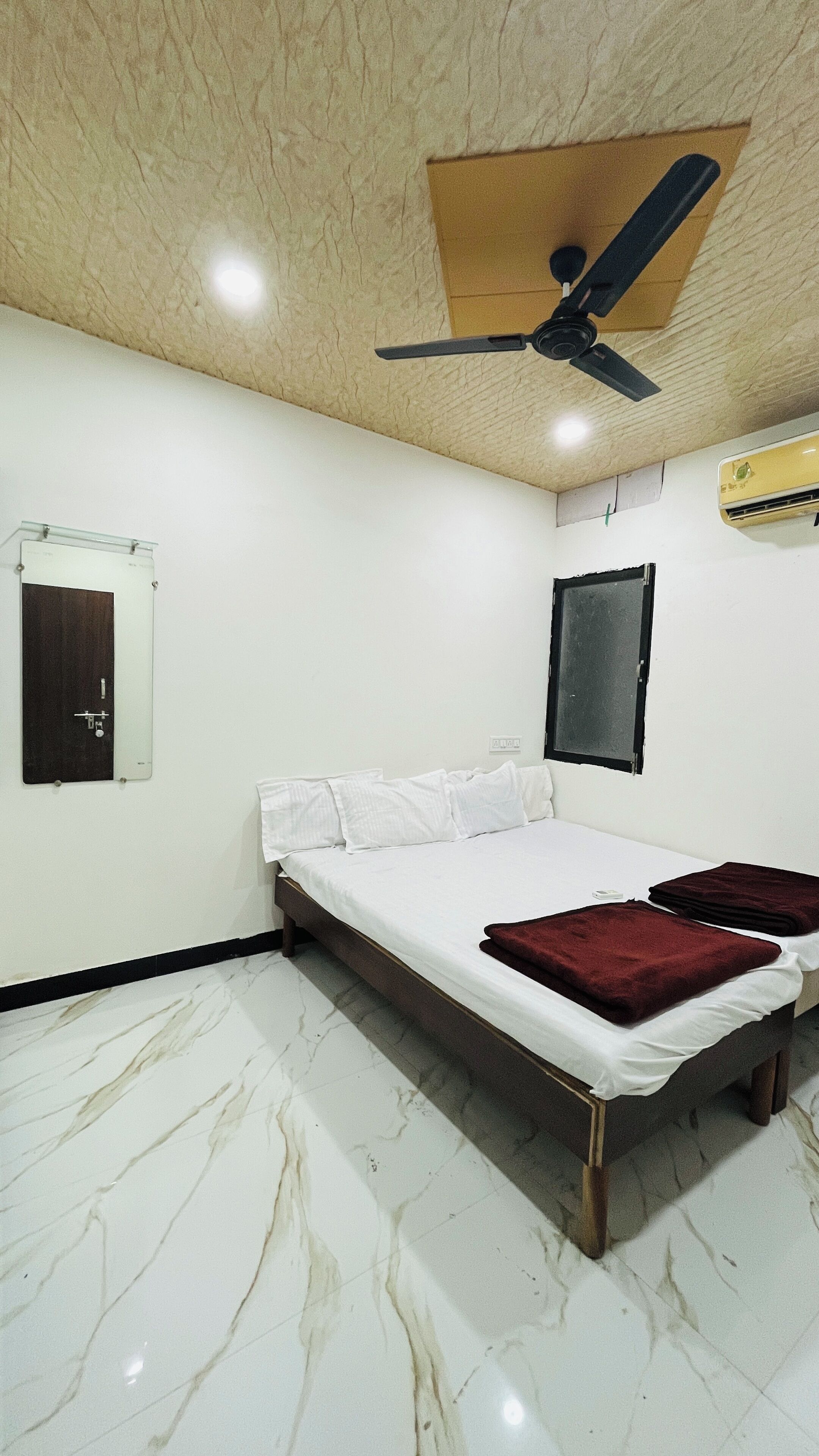 A bedroom with a bed, a ceiling fan, an air conditioner, a mirror, and a door.