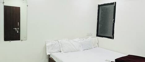 A bedroom with a bed, a ceiling fan, an air conditioner, a mirror, and a door.