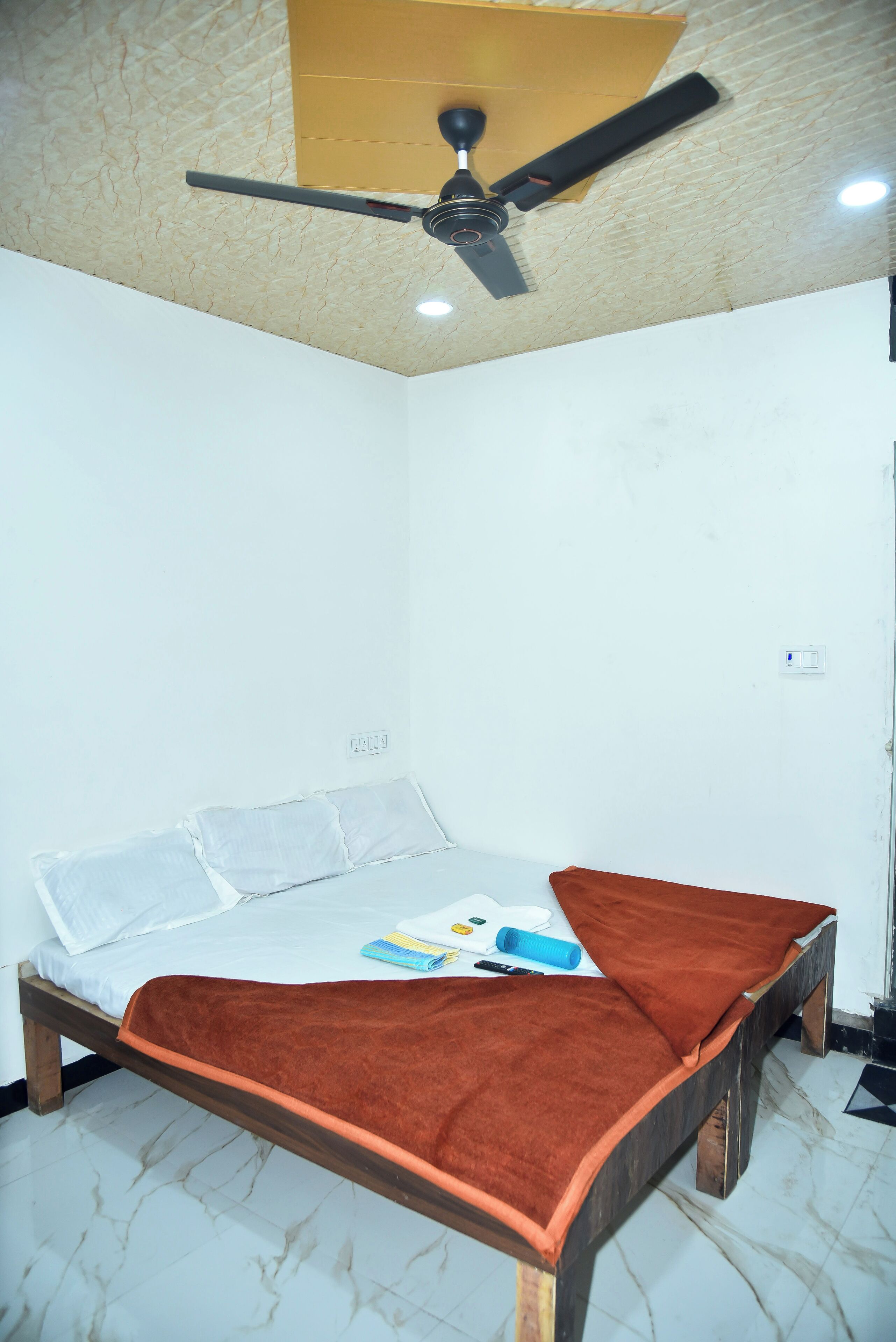 A small, clean room with a single bed, a ceiling fan, and a marble floor.
