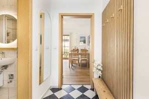 A hallway with a wooden bench, a mirror, and a tiled floor.