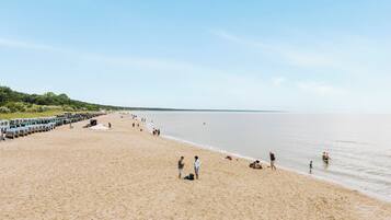 Ein weiter Sandstrand mit Menschen, die herumlaufen und stehen, und eine Reihe Strandliegen auf der linken Seite.