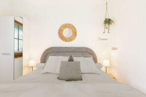 Un dormitorio con cama, lámparas de noche, un espejo redondo y una planta colgante.