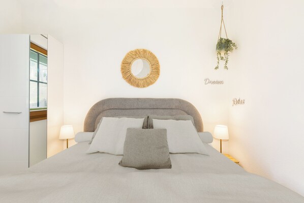 Un dormitorio con cama, lámparas de noche, un espejo redondo y una planta colgante.