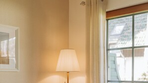 Una habitación con sofá, lámpara de pie, ventana con cortinas e imagen en la pared.