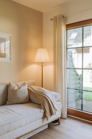 A room with a sofa, a floor lamp, a window with curtains, and a picture on the wall.