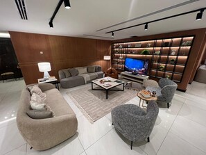 A modern living room with a sectional sofa, armchairs, a coffee table, and a TV against a wooden wall with shelves.