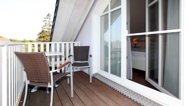 Eine Holzterrasse mit zwei Korbstühlen und einem weißen Geländer.