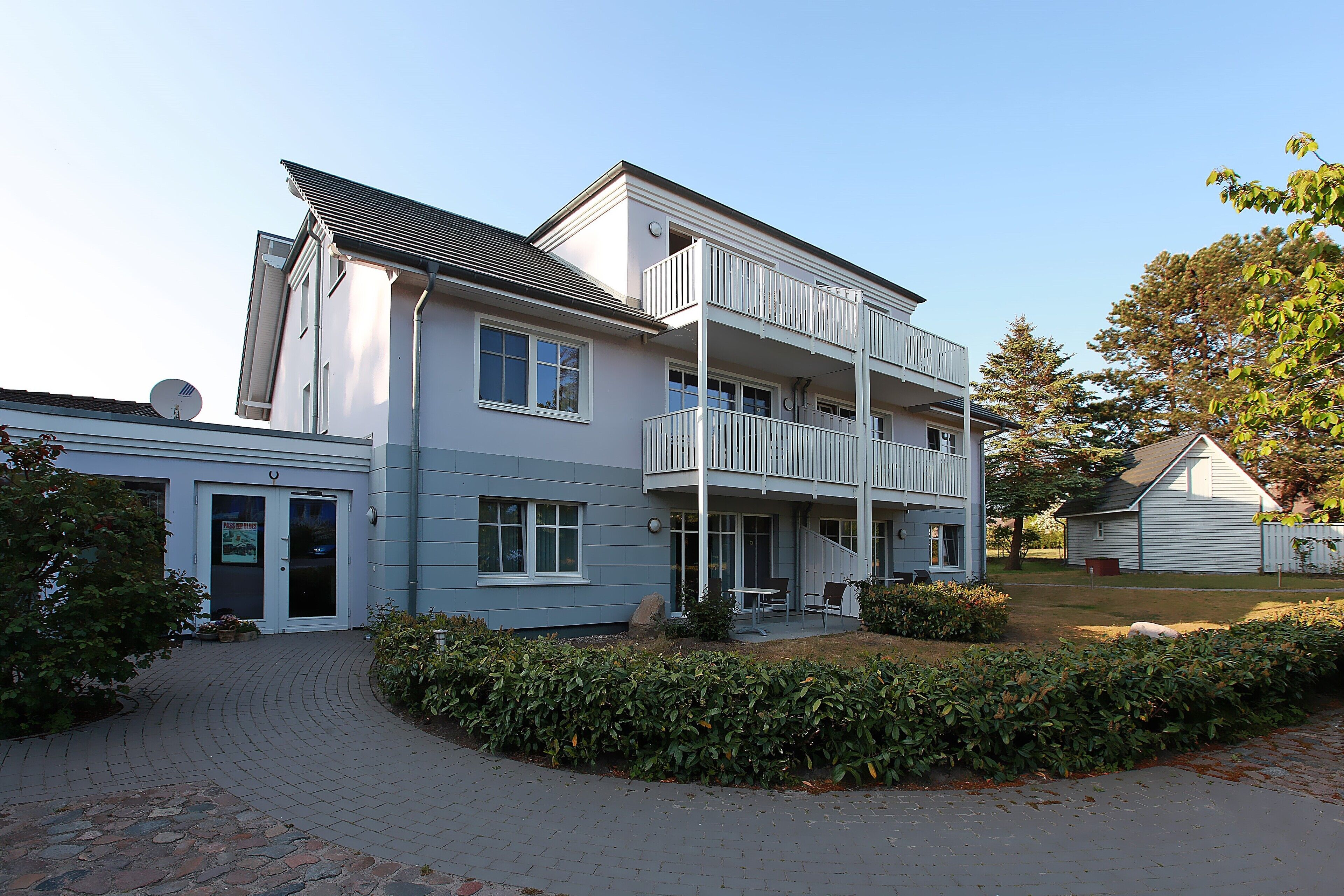 A two-story residential building with a balcony, a satellite dish, and a paved driveway.