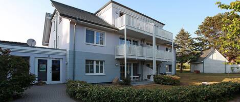 A two-story residential building with a balcony, a satellite dish, and a paved driveway.
