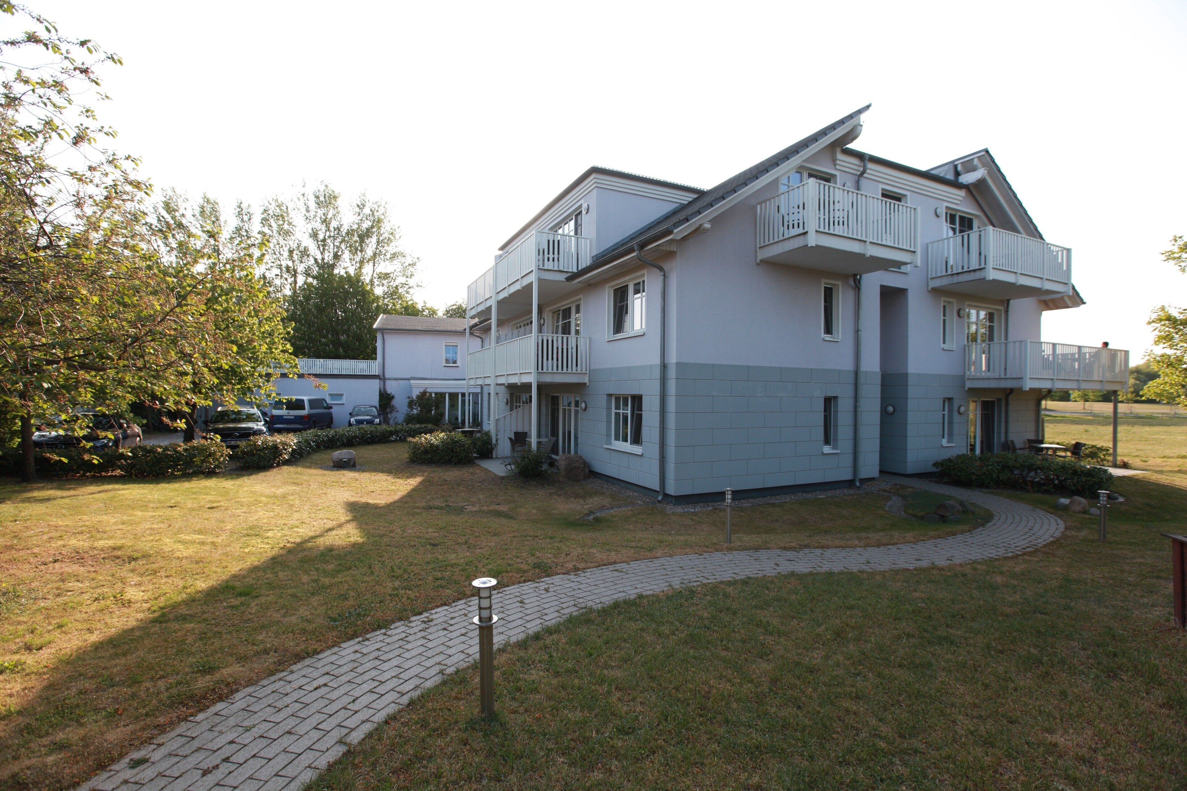 En moderne boligbygning i to etager med en facade i grå og hvid, en belagt indkørsel og et lille haveareal.