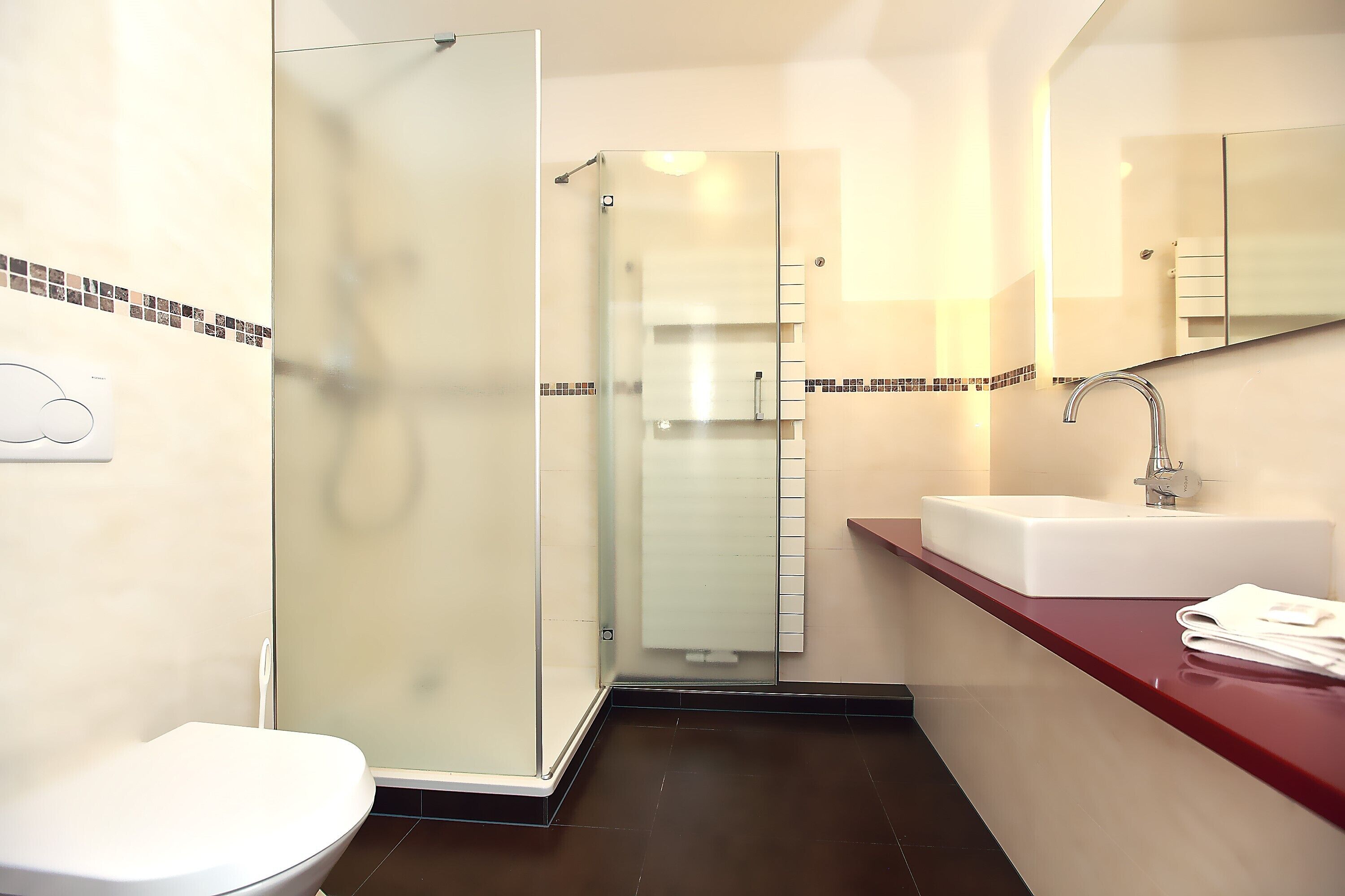 A modern bathroom with a glass-enclosed shower, a white sink, and a red countertop.