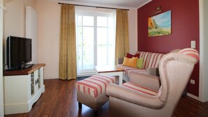 Een woonkamer met een televisie, een bank, een salontafel en een schilderij aan de muur.