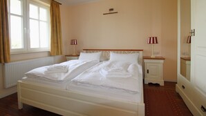 A hotel room with a double bed, two bedside tables with lamps, a radiator, and a window with curtains.